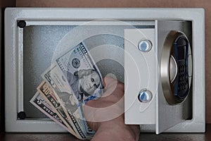 Close-up of a man`s hand putting American dollars in a safe Deposit box. Banknotes of 5, 10, 20, 100 US dollar. Storage of money,
