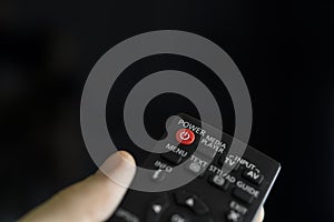 Close up on a man`s hand with the remote control want switch on the TV and presses the button on the remote control