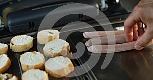 Close up on man's hand roasting bruschetta and sausages on the barbecue gas grill outdoor in the backyard