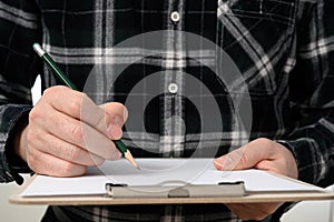 A close-up of a man`s hand signing a document with a clipboard