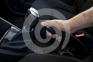 Close up of a man\'s hand tightens the manual handbrake on the car