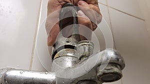 Close-up of a man's hand turning the broken lever of a water faucet