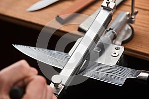 Close-up on man& x27;s hand using a manual machine to sharpen a Japanese knife