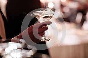 A close up of a man`s hand who is dressed in formal attire and holding a martini glass on party background