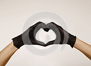 Close up man`s hands in black protective gloves making heart sign with hands over white background. Valentine`s Day, 8th March,