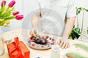 Close-up of a man& x27;s hands decorating a chocolate heart cake with a sprig of fresh mint for valentine& x27;s day