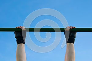 Close-up of a man`s hands in gloves playing sports on a horizontal bar against a blue sky