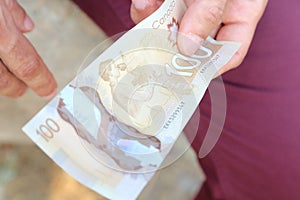 A close up of a man`s hands holding Canadian money- $100 bill