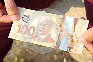 A close up of a man`s hands holding Canadian money- $100 bill