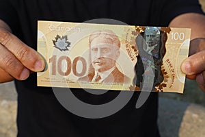 A close up of a man`s hands holding Canadian money- $100 bill