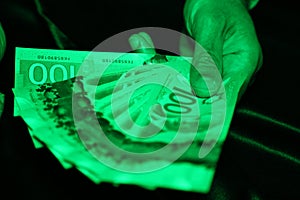 A close up of a man`s hands holding Canadian money under a green light- $100 bill