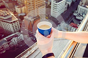 Close up man`s hands holding take away paper cup with morning hot drink - coffee or tea with inspiring view on abstract city back