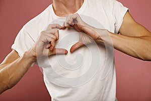 Close up man`s hands making heart sign with hands over pink background. Valentine`s Day, 8th March, anniversary romantic concept