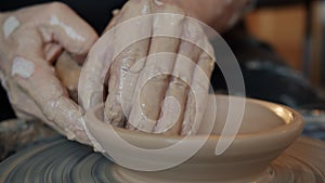 Close-up of man`s hands molding clay making bowl on spinning wheel in workshop