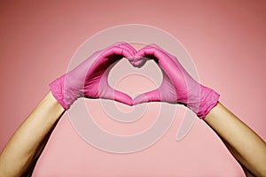Close up man`s hands in pink protective gloves making heart sign with hands over pink background. Valentine`s Day, 8th March,