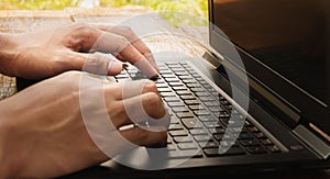 Close-up of man's hands typing on a laptop computer keyboard and surfing the internet on a table.