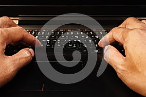 Close-up of man's hands typing on a laptop computer keyboard and surfing the internet on a table.