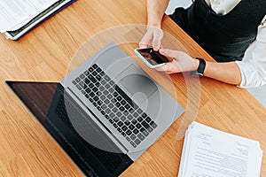 Close up of man's hands typing on a laptop keyboard and holding a smartphone