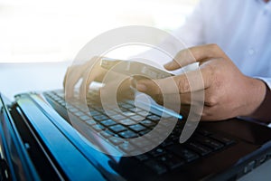 Close up Man`s hands typing on laptop keyboard and using smart phone