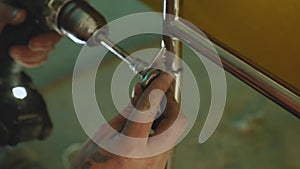 A close-up of a man's hands with a wrench and an electric screwdriver tightens a nut on a stainless steel structure