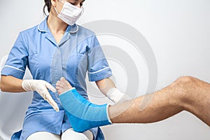 Female doctor in a blue medical gown checking broken leg on male patient