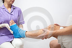 Female doctor in a blue medical gown checking broken leg on male patient