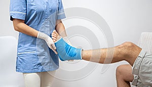 Female doctor in a blue medical gown checking broken leg on male patient