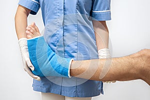 Female doctor in a blue medical gown checking broken leg on male patient