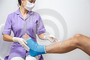 Female doctor in a blue medical gown checking broken leg on male patient