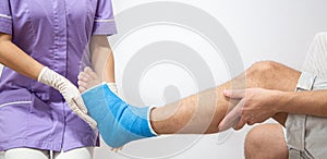 Female doctor in a blue medical gown checking broken leg on male patient