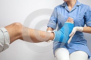 Female doctor in a blue medical gown checking broken leg on male patient