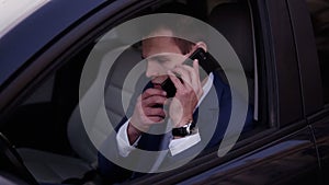 Close-up of a man sitting in the car on a driver`s seat, holding a smartphone. Businessman talking while sitting in a