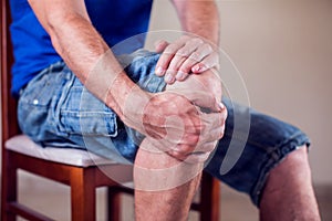 Close up of a man sitting and holding his knee in pain due to injury on white background. Healthcare, medicine, people concept