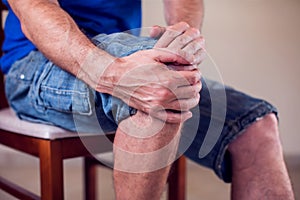 Close up of a man sitting and holding his knee in pain due to injury on white background. Healthcare, medicine, people concept