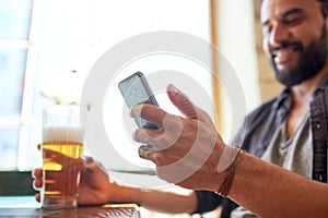 Close up of man with smartphone and beer at pub