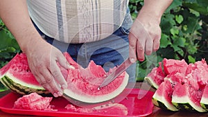 A close-up man takes out the bones from a slice of watermelon with a knife.
