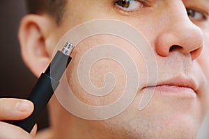 close-up. a man with trimmers for cutting hair in nose and ears.