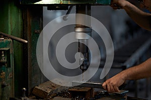 Close up of man using drill press for making holes in metal