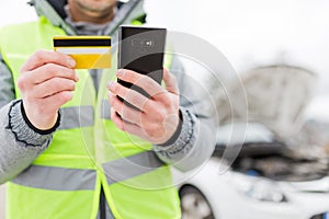 Close up of man using mobile phone and roadside assistance insurance membership card next to broken car