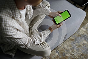 Close up of a man using mobile smart phone with green screen sitting in living room on sofa