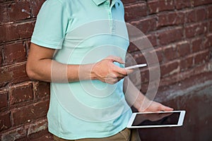 Close up of a man using mobile smart phone and tablet, background brick wall