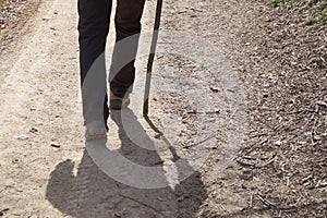 Close-up of a man walking along a dirt road leaning on a wooden stick