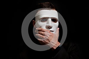 Close-up of a man in a white mask, surprise, thoughtfulness. Touches a hand to the mask photo