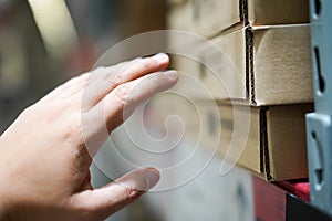 Close up the man who reaches his hand to furniture in a brown paper box on shelf in the warehouse