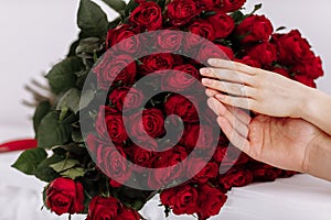 close-up of man and woman hands with engagement rings. Hands of the on the background of the big bouquet of red roses