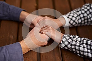 Close up on a man and a woman holding hands at a wooden table. Loving couple holding hands on table, man friend husband