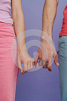 Close up man and woman holding pinkies while standing isolated over purple background