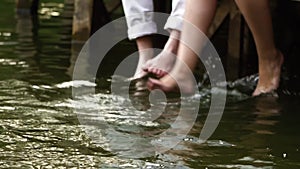 Close up. Man and woman kick in the water. Bare feet touch the water in the lake. Bare feet. Lake