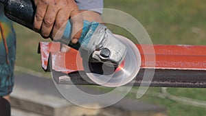 Close-up of man in working clothes cutting a list of red steel roofing by metal cutting saw. Clip. Materials and