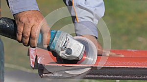 Close-up of man in working clothes cutting a list of red steel roofing by metal cutting saw. Clip. Materials and